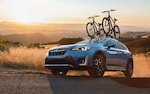 A 2021 Crosstrek Hybrid with mountain bikes mounted to a rack accessory on its raised roof rails driving up a rough country road.