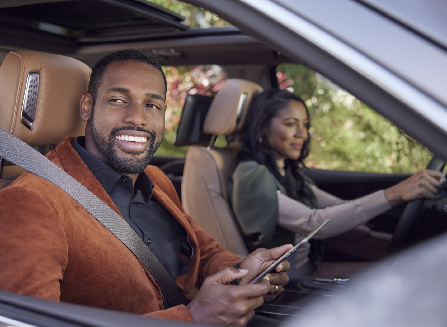 Couple in a car with the woman driving and the man smiling holding a tablet device
