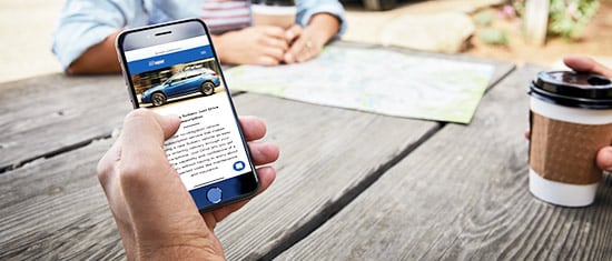 Group sitting at picnic table with Just Drive Subscription App on Phone