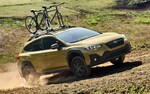 A 2021 Subaru Crosstrek Sport with mountain bikes on its standard raised roof rails driving on a dirt road.
