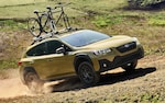 A 2021 Subaru Crosstrek Sport with mountain bikes on its standard raised roof rails driving on a dirt road.