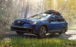 A 2021 Subaru Outback driving on a backcountry road with a cargo carrier on its standard raised roof rails.
