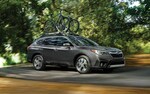 A 2021 Subaru Outback driving on a country road with two mountain bikes racked on its standard raised roof rails.