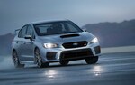2021 WRX STI driving on a race track with the headlights illuminated.